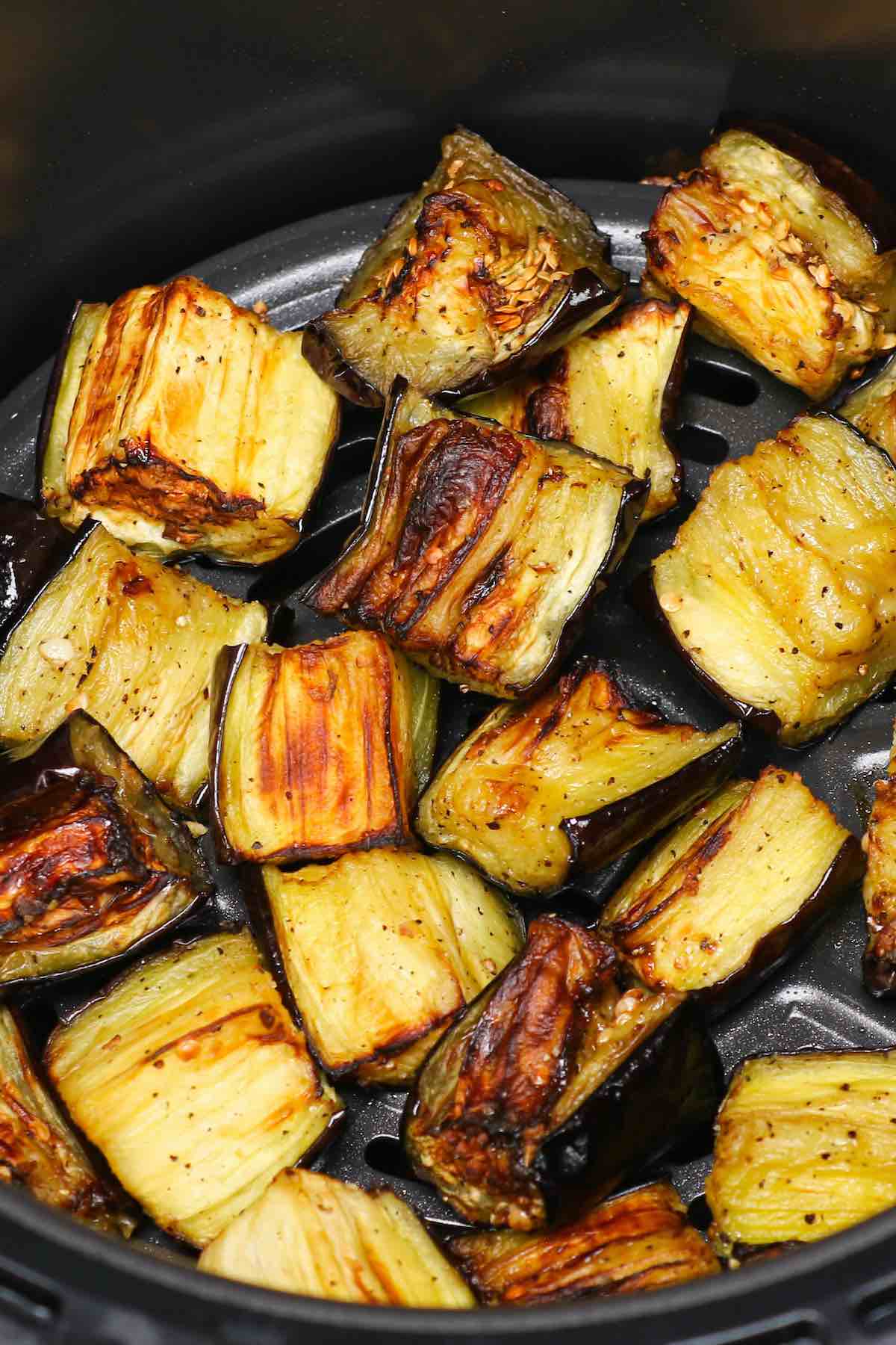 Beautifully caramelized pieces of seasoned eggplant in an air fryer basket #AirFryerEggplant