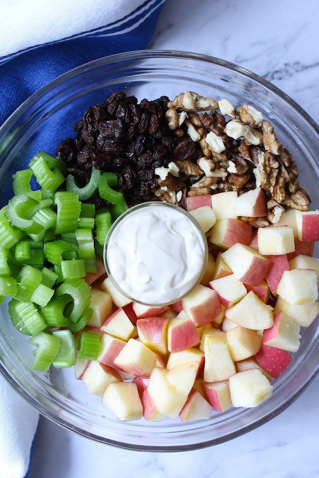 Chopped apples, celery, walnut pieces, raising and a mayonnaise dressing in a mixing bowl