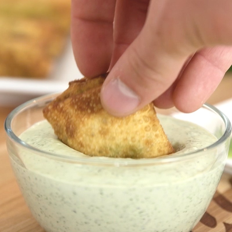 Dipping an avocado egg roll in the creamy jalapeño dipping sauce