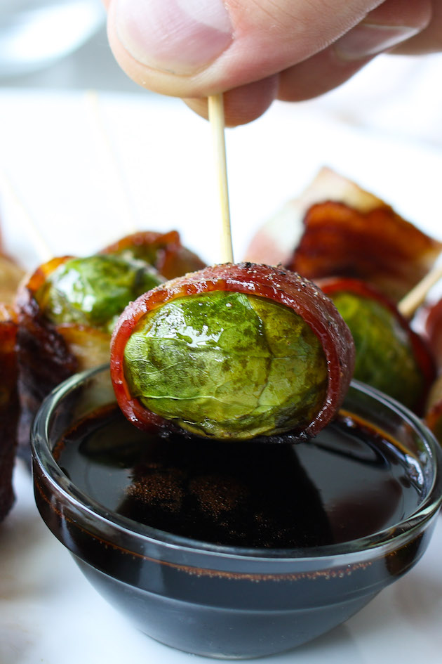 A bacon wrapped brussel sprouts being dipped into a balsamic dressing for the perfect hors d'oeuvre