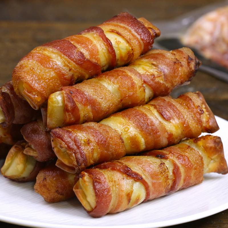 This is a closeup photo of bacon-wrapped spring rolls served in a stack on a plate