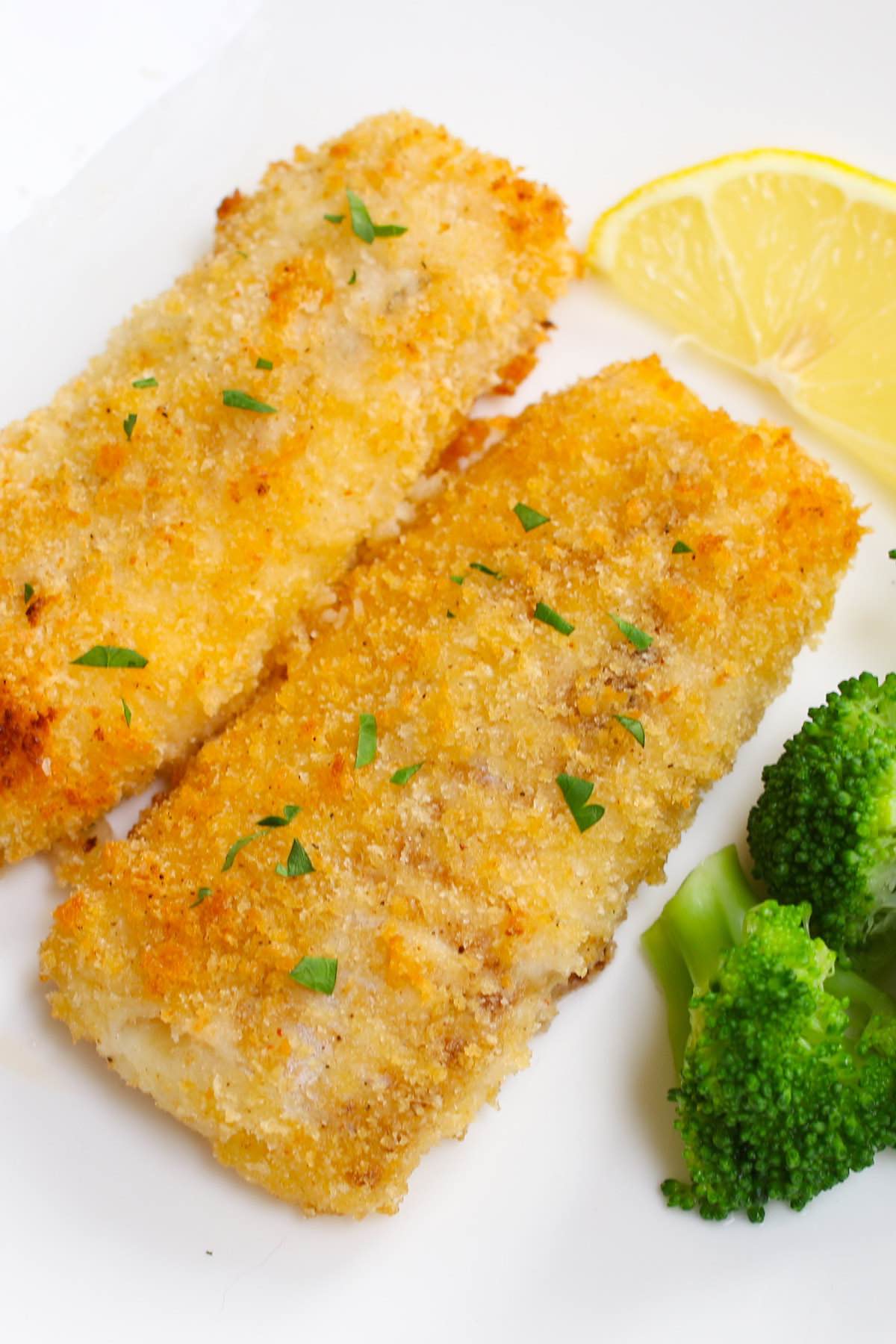 Baked breaded haddock fillets garnished with fresh lemon and served with a side of broccoli 