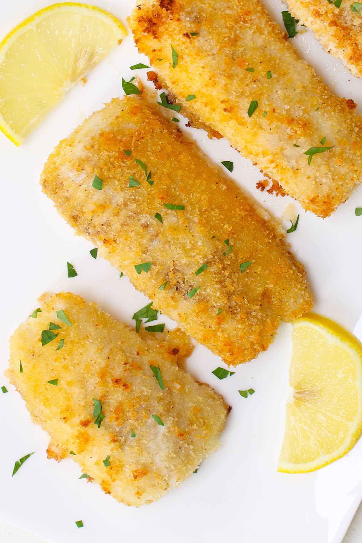 Breaded fish fillets that have turned a beautiful golden brown in the oven, garnished with minced parsley and lemon wedges
