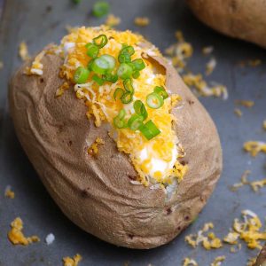 A perfect baked potato topped with sour cream, grated cheese and green onion