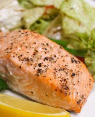 Serving of portion-size baked salmon fillet with a side salad on a serving plate with a lemon wedge