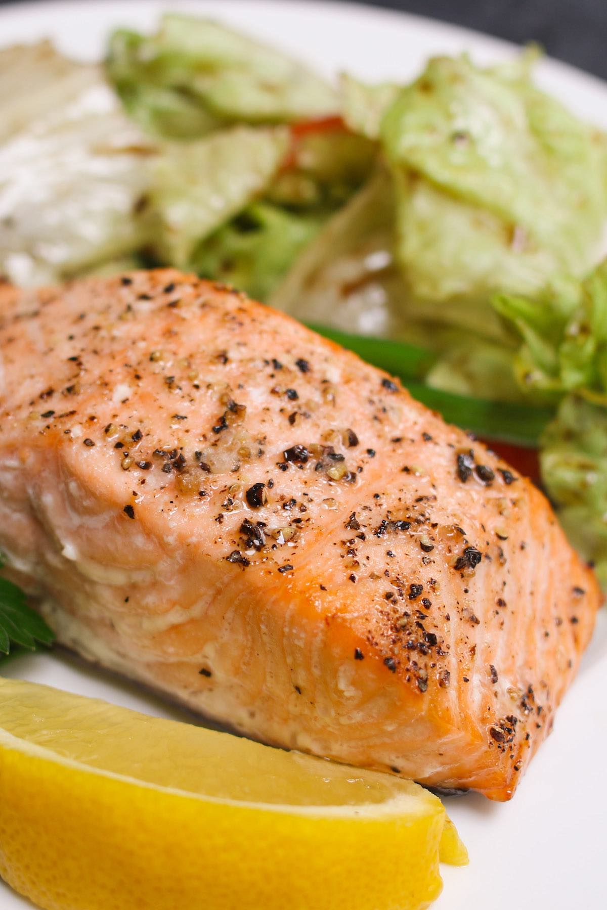 Closeup of baked fish with freshly cracked pepper on top and served with a side salad