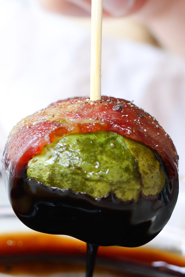 Closeup of a bacon wrapped Brussel sprout on a toothpick dipped in balsamic glaze