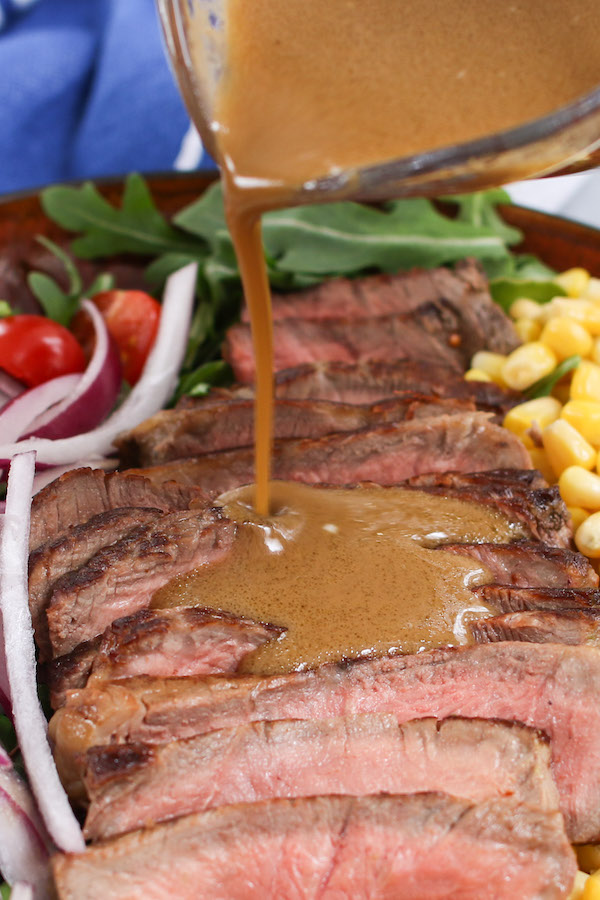 Balsamic vinaigrette dressing being poured onto steak salad