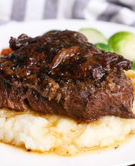 A braised beef cheek on a bed of mashed potatoes with Brussel sprouts