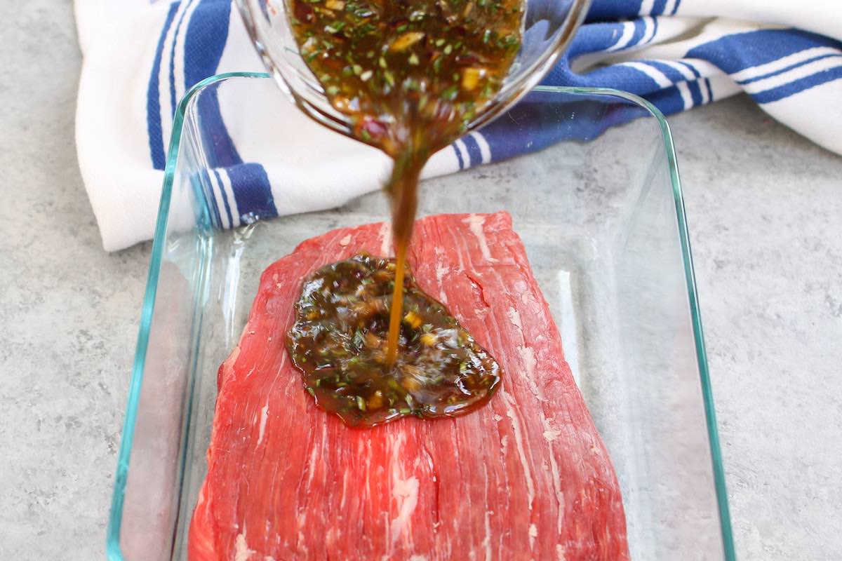 Pouring the marinade mixture on top of flank steak in the container.
