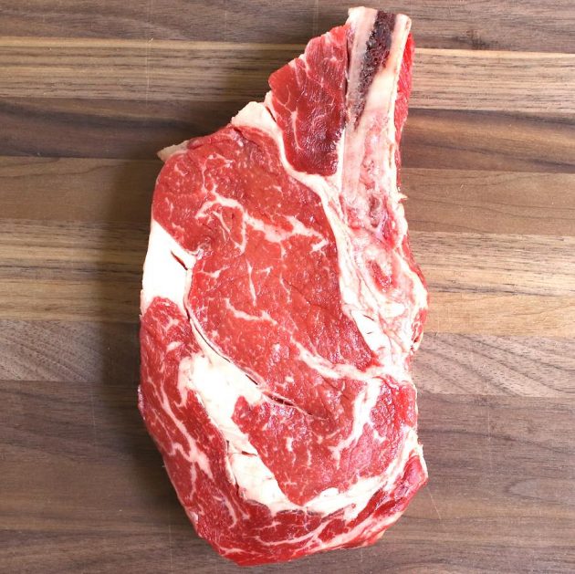 A thick bone-in ribeye steak before cooking, showing its beautiful marbling
