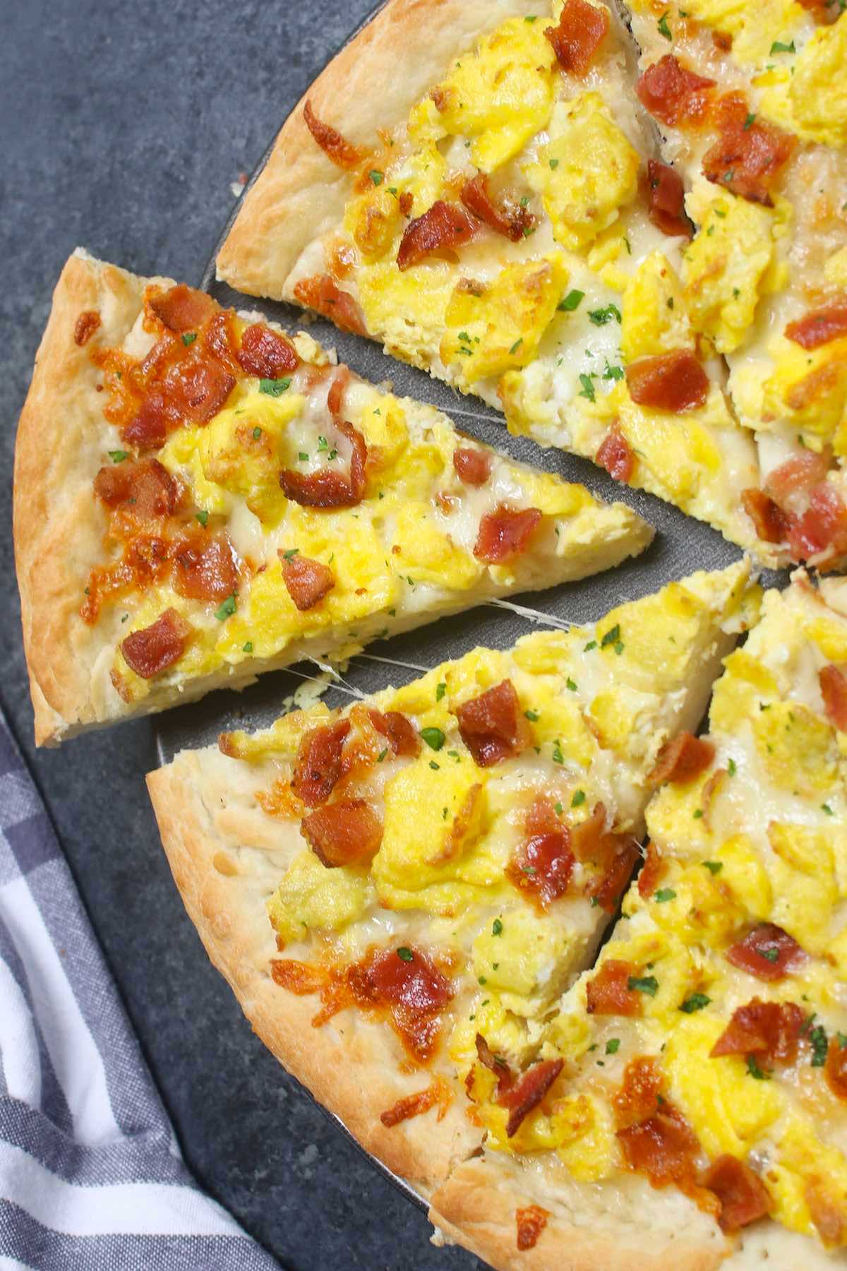 Easy Breakfast Pizza recipe begins with homemade pizza dough, topped with crisp bacon bits, scrambled eggs and mozzarella cheese.