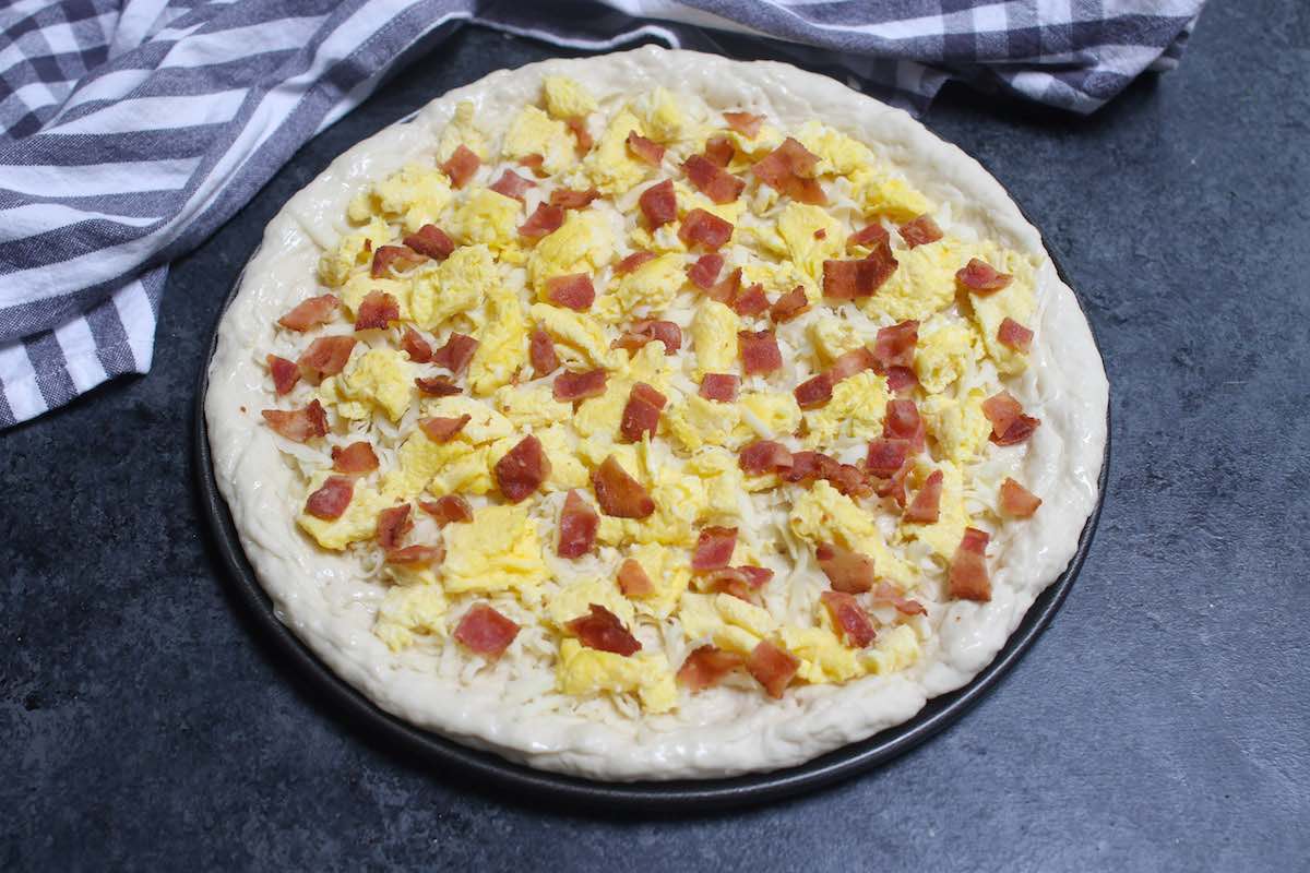 Crumbled bacon, scrambled eggs and mozzarella cheese on pizza dough