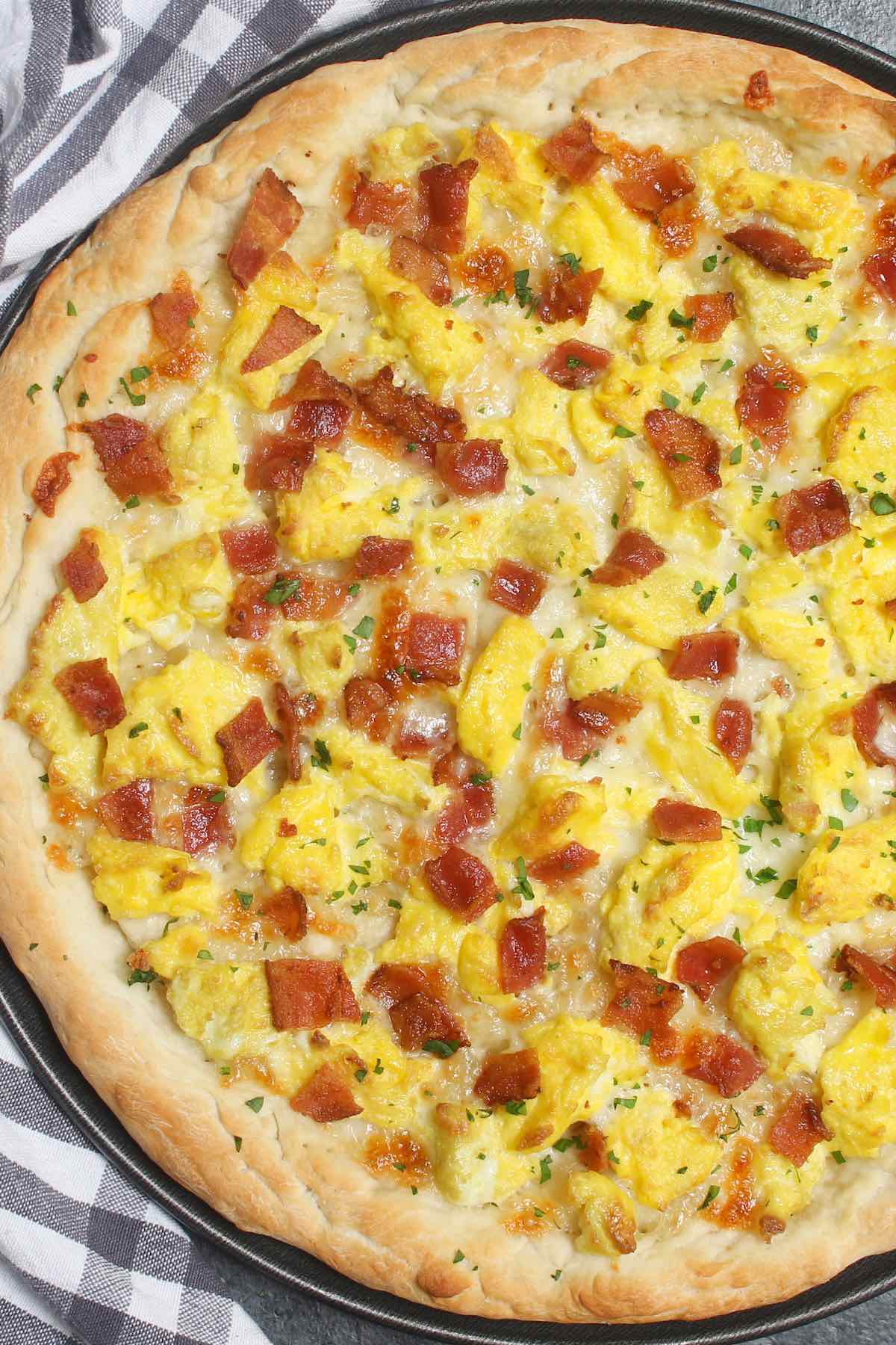 Easy Breakfast Pizza recipe begins with homemade pizza dough, topped with crisp bacon bits, scrambled eggs and mozzarella cheese. 
