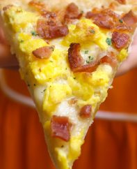 This easy Breakfast Pizza recipe begins with my homemade pizza dough, topped with crisp bacon bits, scrambled eggs and mozzarella cheese. With a few tips, you can make it fast to feed the whole family on busy mornings. Here you’ll learn everything to make the best bacon pizza!