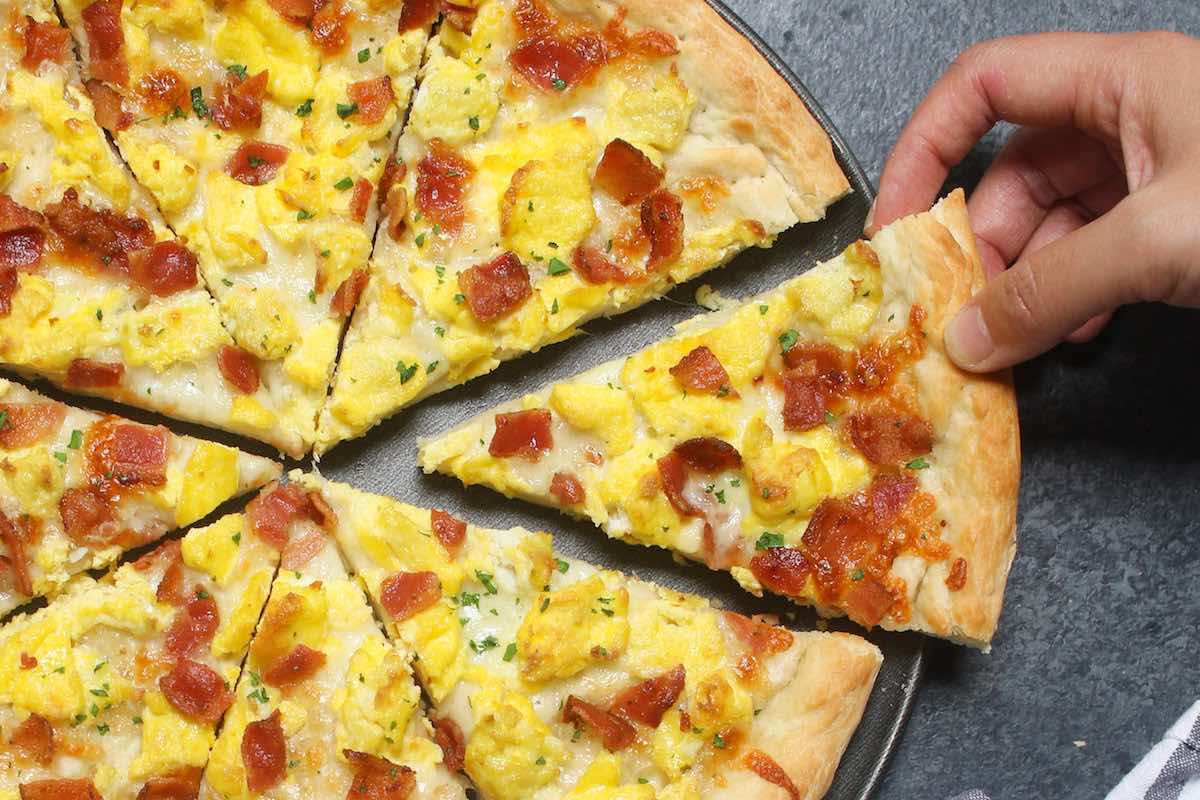Easy Breakfast Pizza recipe begins with homemade pizza dough, topped with crisp bacon bits, scrambled eggs and mozzarella cheese. 
