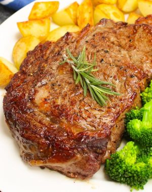 Perfectly broiled steak served with potatoes and broccoli on a serving plate with a sprig of rosemary for garnish.