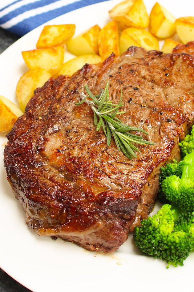 Perfectly broiled steak served with potatoes and broccoli on a serving plate with a sprig of rosemary for garnish.