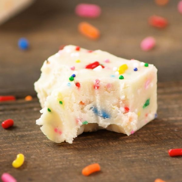 Cake Batter Fudge - this photo shows a square piece of fudge on a wooden serving plate with two bites taken and two more left. 