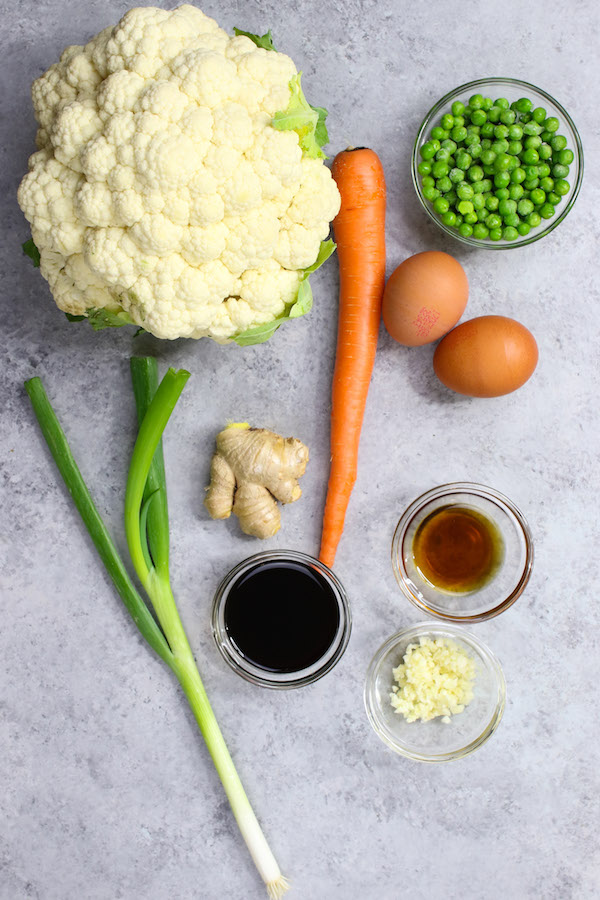 Cauliflower rice is made with simple ingredients including fresh cauliflower and optional carrot, green onion, peas, eggs and seasonings for flavor