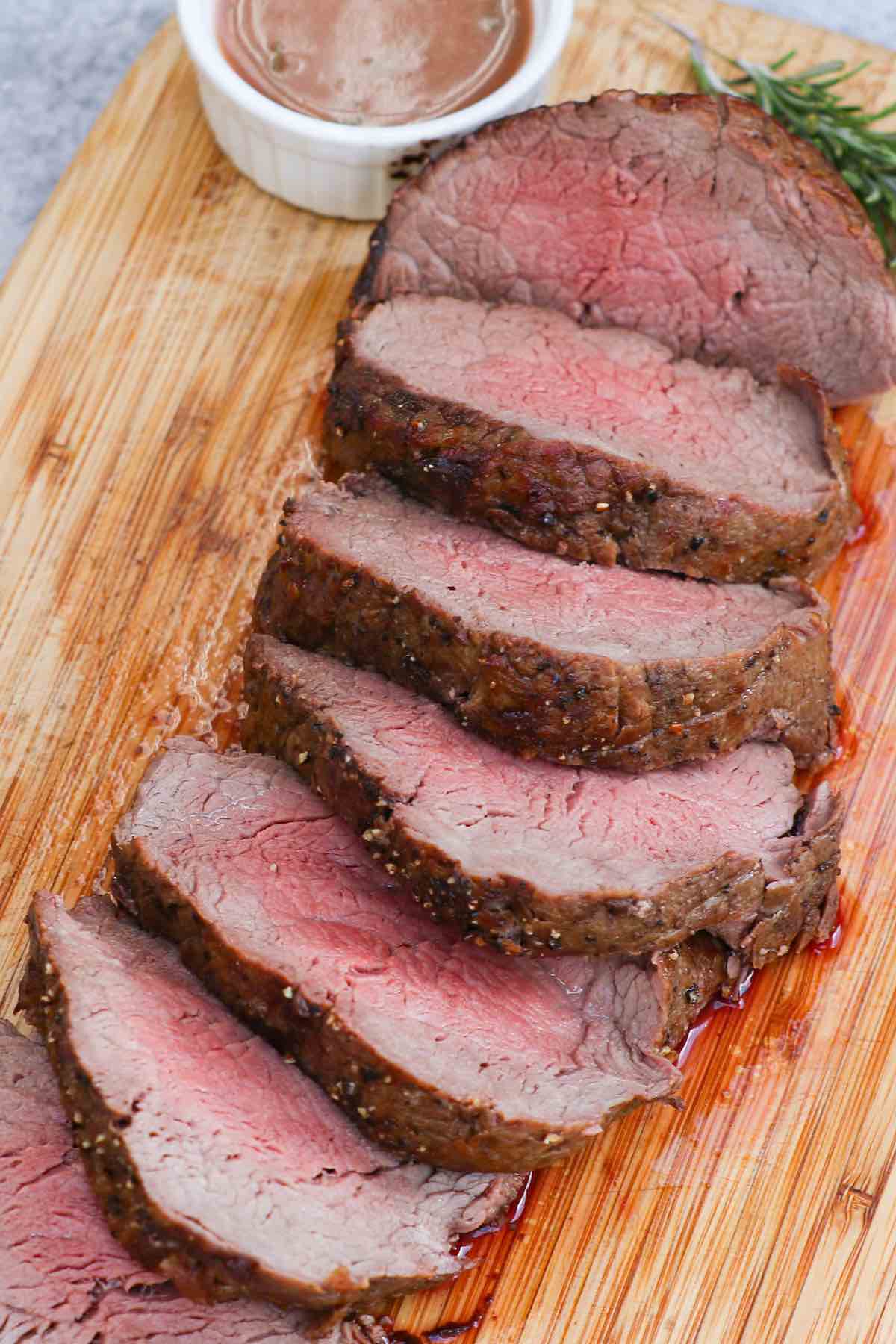 Slices filet mignon roast cooked medium on a carving board with homemade sauce and fresh rosemary