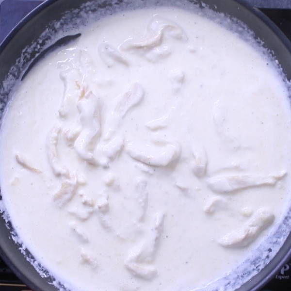 Adding cream sauce to strips of sauteed chicken in a skillet