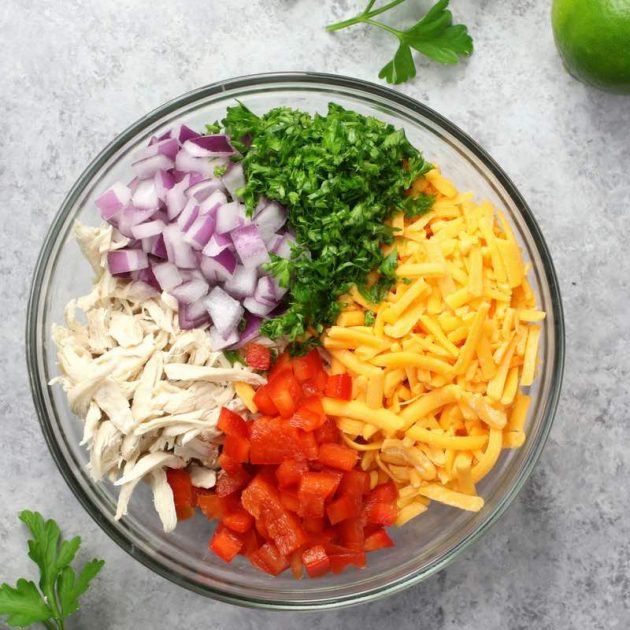 Shredded chicken with red onion, minced parsley, shredded cheese and chopped red bell pepper in a mixing bowl