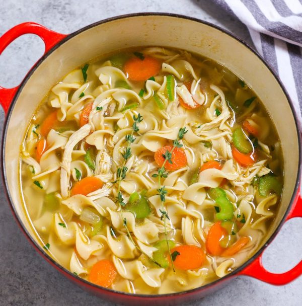 Overhead of Homemade Chicken Noodle Soup in an enamelled soup pan with sprigs of fresh thyme on top