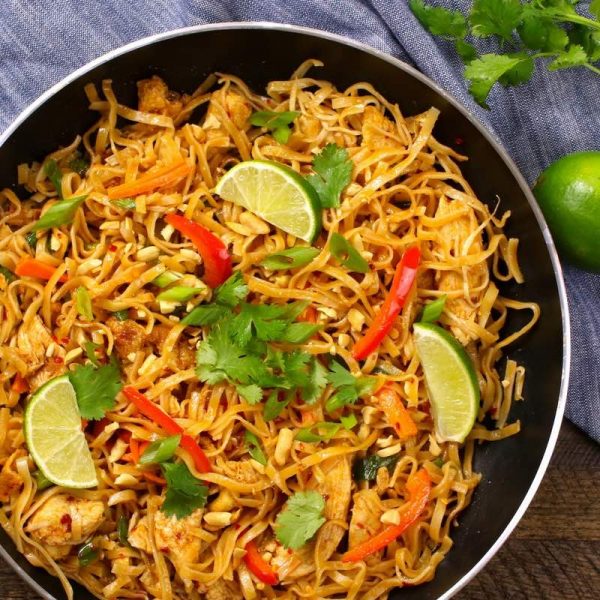 Chicken Pad Thai - this photo shows this classic chicken pad thai recipe in a skillet garnished with lime wedges and cilantro and ready to be served
