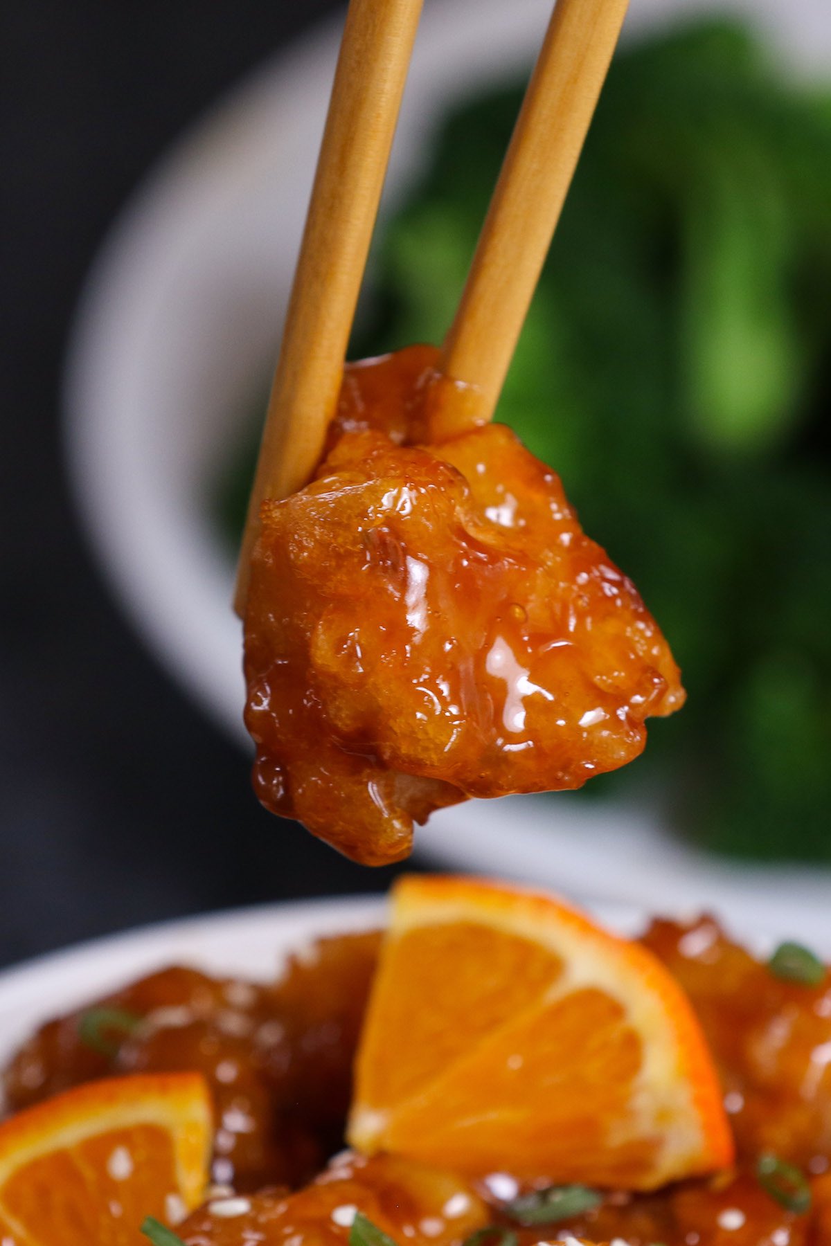 Close-up of chopsticks picking up a piece of deep fried chicken coated in sticky sauce