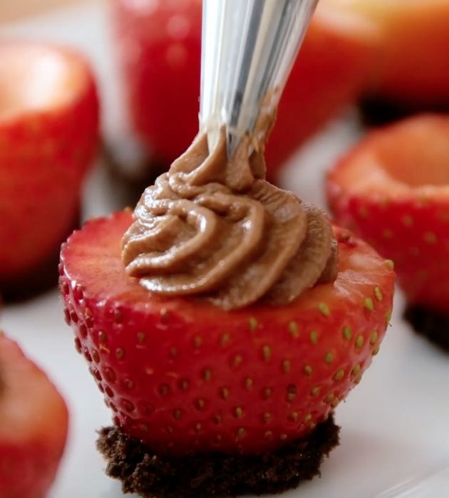 Piping cheesecake filling into a strawberry