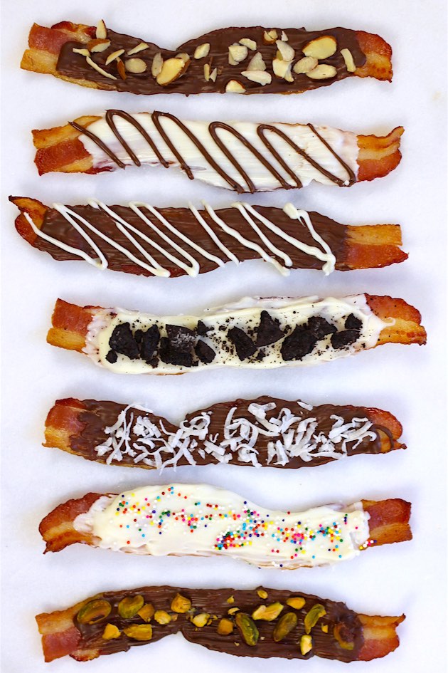 Overhead view of chocolate covered bacon made six ways with semisweet chocolate, white chocolate and toppings including pistachios, including with dark chocolate, white chocolate and toppings including pistachios, shredded coconut and sprinkles