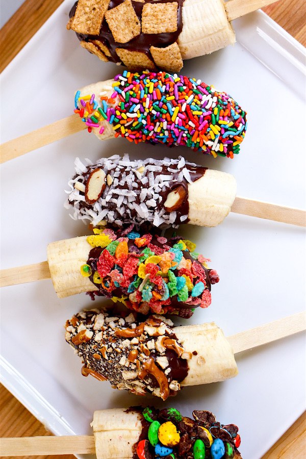 Chocolate Covered Bananas are the easiest snacks ever! Just 3 ingredients: banana, chocolate and coconut oil, plus whatever toppings you like such as crushed M&Ms, fruity pebble cereal, cinnamon toast crunch and colored sprinkles. Beautiful and irresistibly delicious! Quick and easy recipe. Kids friendly. Video recipe. | Tipbuzz.com #ChocolateCoveredBananas #ChocolateBananas