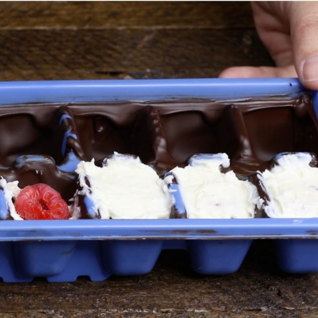 This photo shows filling ice cube tray cups with creamy cheesecake filling and fresh raspberries when making Cheesecake Bites