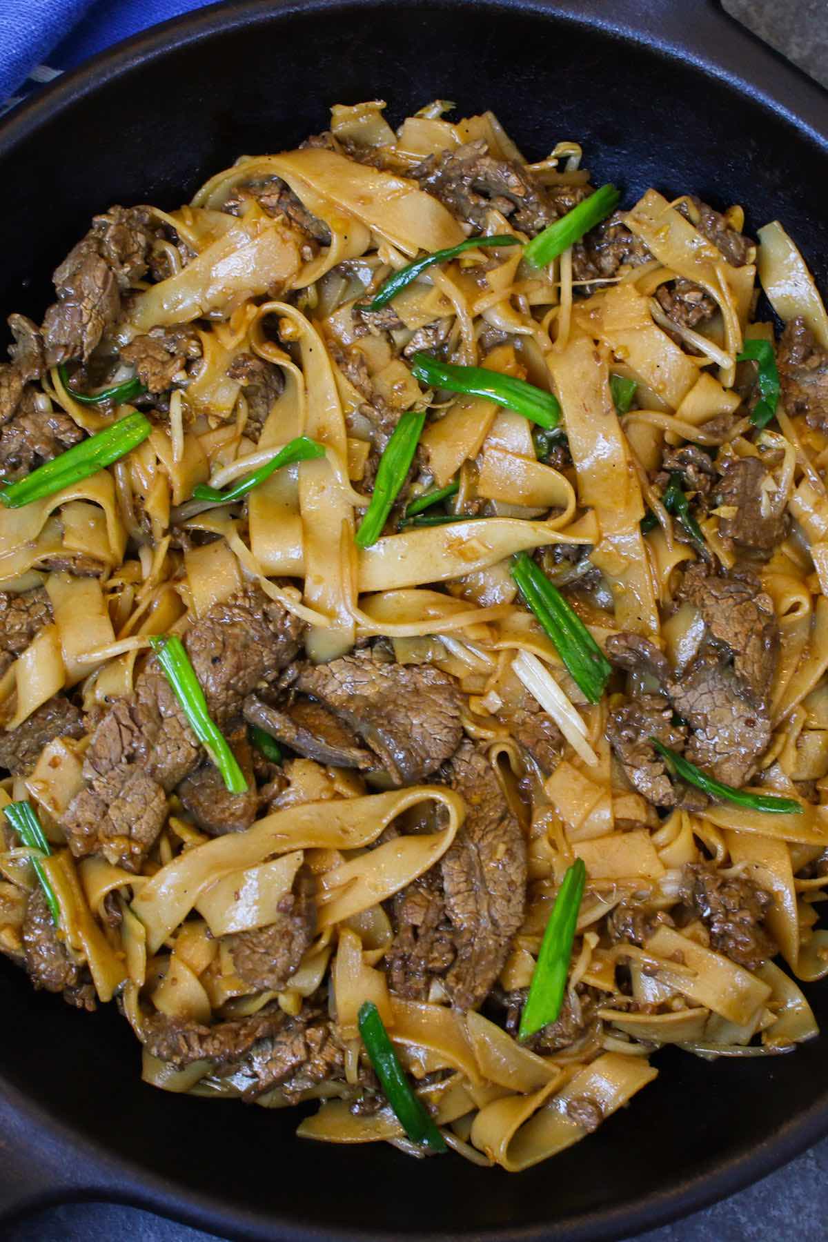 Beef chow fun noodles in a wok after being prepared showing tender strips of beef and fresh green onions for garnish