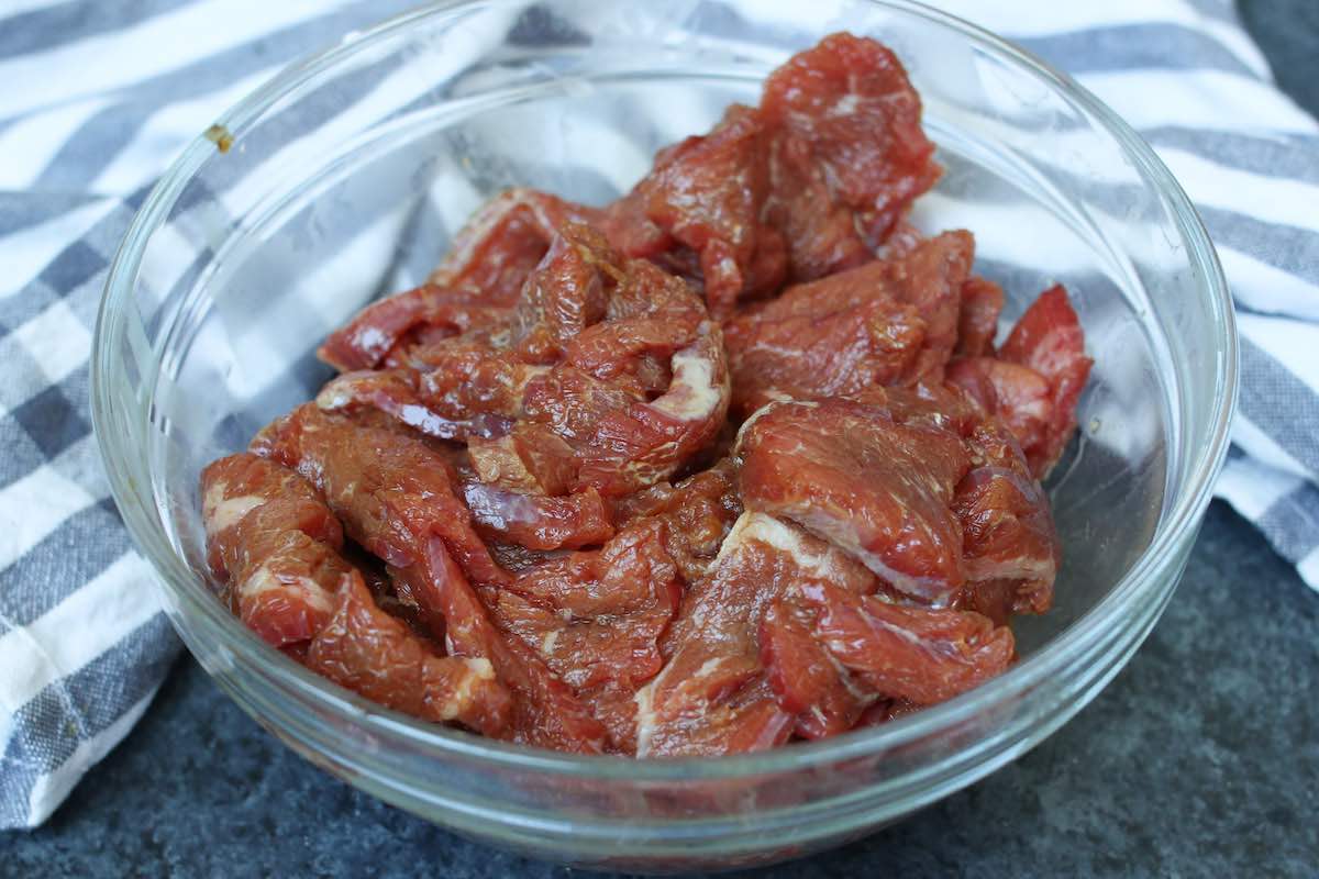 Strips of beef marinating in a soy sauce mixture in a bowl