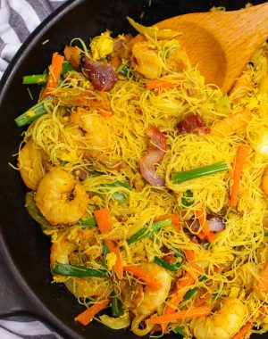 Singapore chow mei fun in a skillet showing thin rice noodles, shrimp, pork and vegetables in a characteristic yellow color