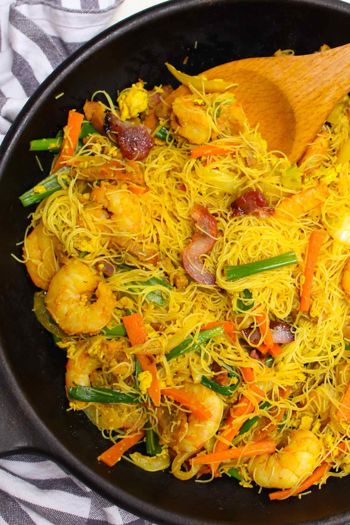 Singapore chow mei fun in a skillet showing thin rice noodles, shrimp, pork and vegetables in a characteristic yellow color 