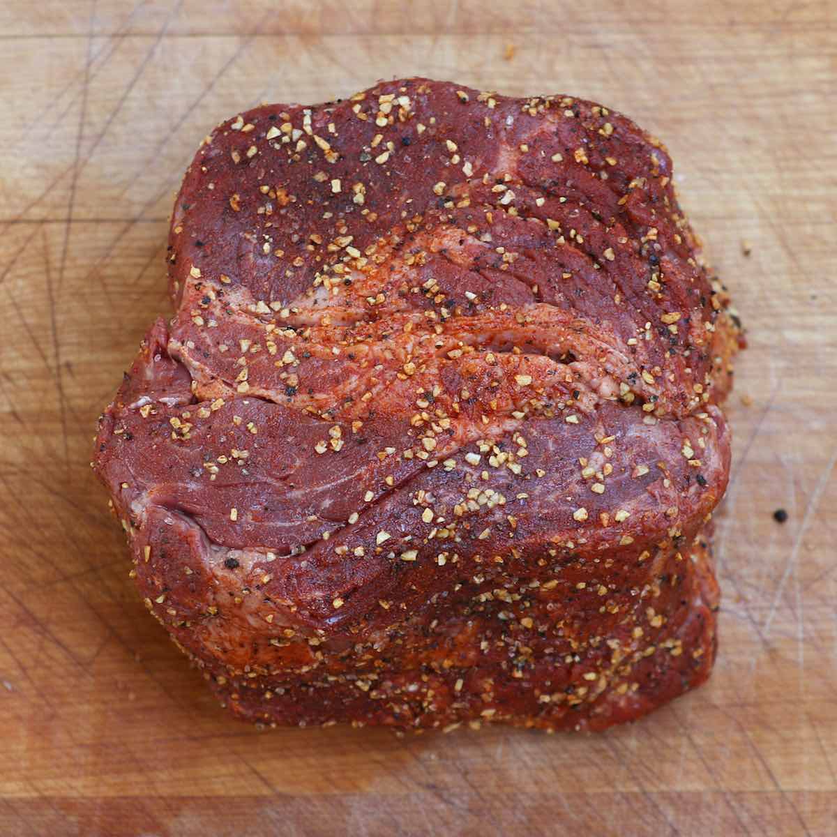 A square cut of chuck roast rubbed with seasonings and showing its beautiful marbling underneath