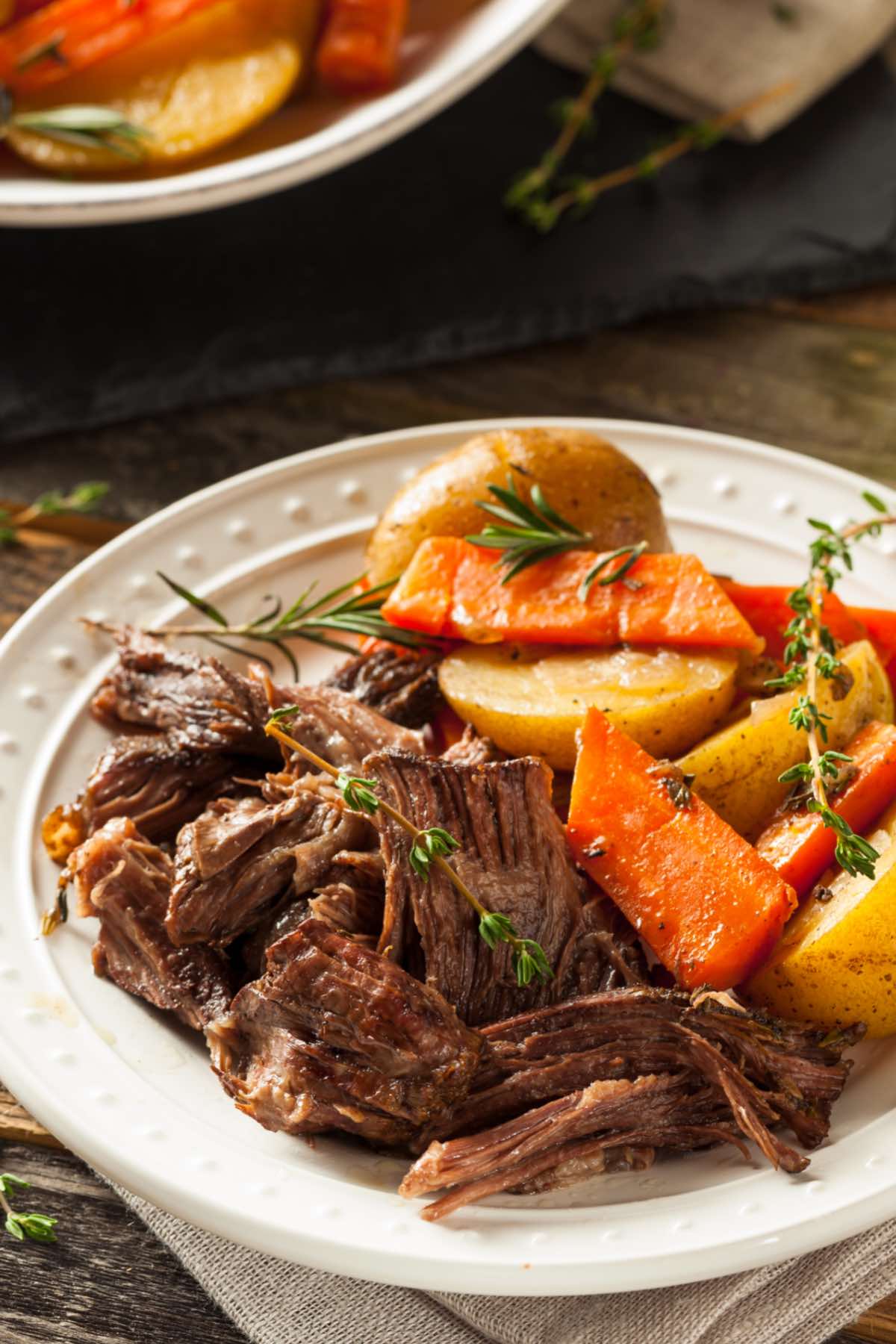 Chuck roast cooked in the oven as a pot roast and served shredded with vegetables on a plate