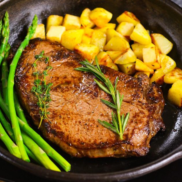 Cooked Sirloin steak with potatoes and asparagus in a cast-iron skillet