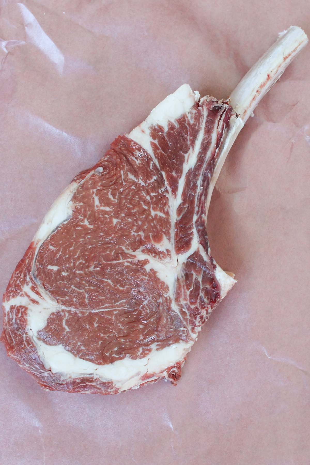 Raw cowboy steak showing the frenched bone and marbling of the meat