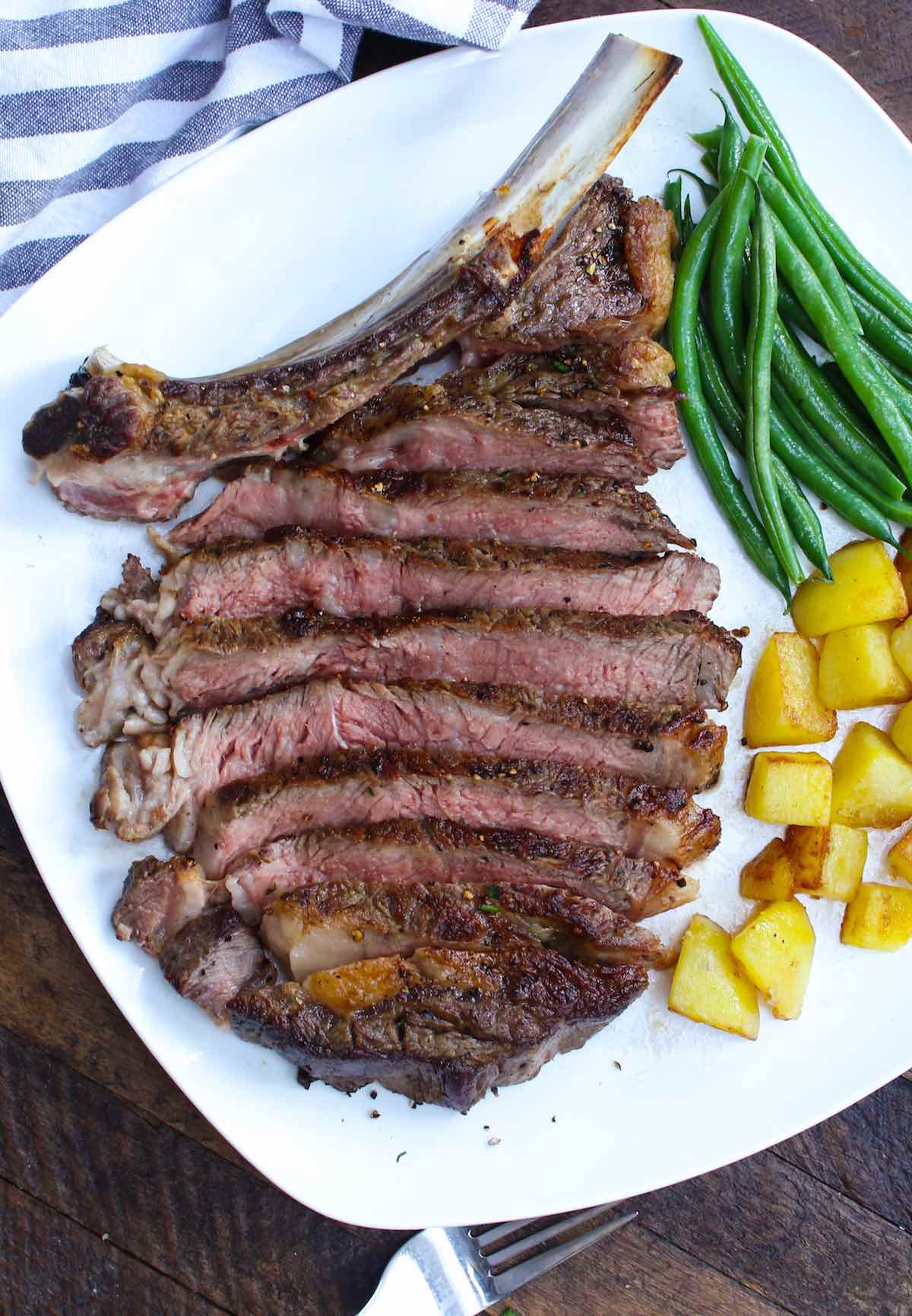 Sliced cowboy ribeye steak on a serving plate 