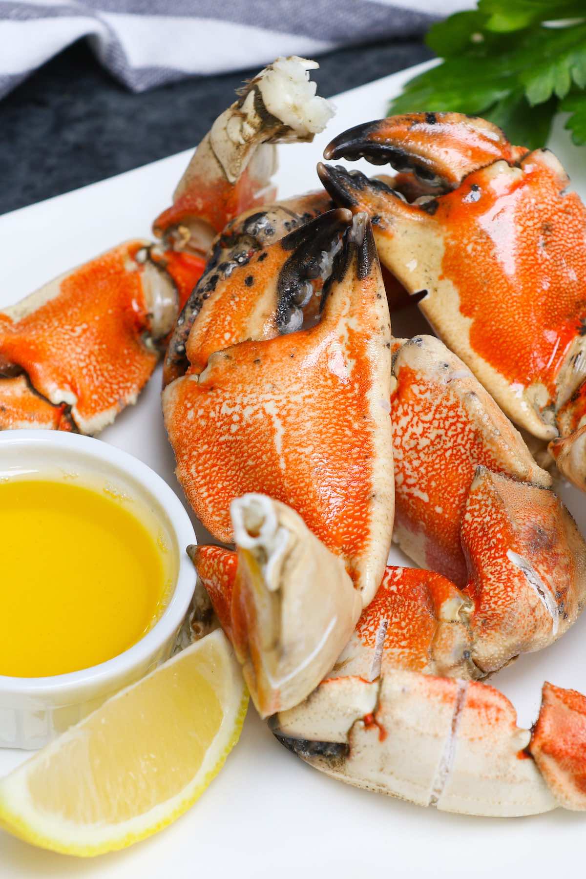 Steamed Jonah crab claws on a serving platter with melted butter and lemon wedges