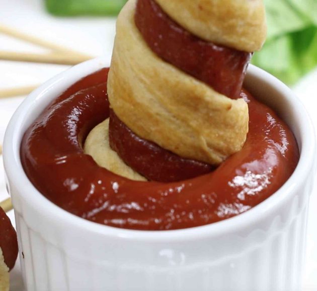 Close-up of dipping a crescent roll hot dog in ketchup - a mouthwatering party appetizer you can make with just 3 ingredients