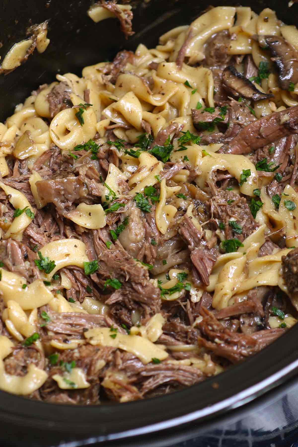 Beef and noodles in the crock pot garnished with fresh parsley