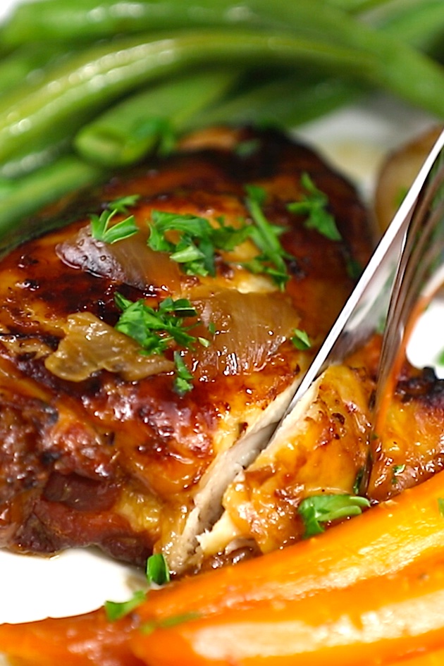 Cooked chicken thighs served on a white plate with carrots, potatoes and green beans