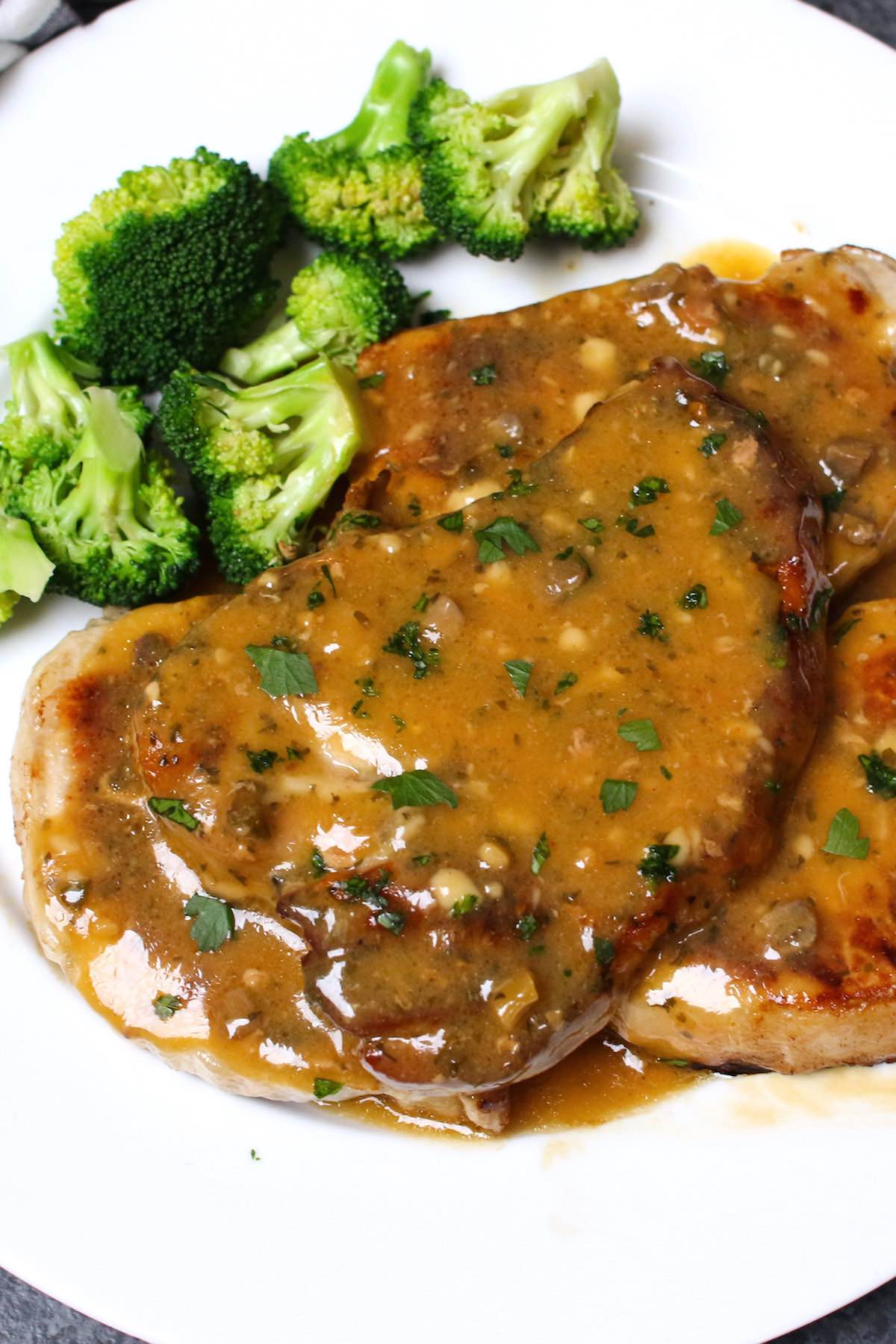 Crockpot ranch pork chops on a serving plate garnished with parsley and served with broccoli