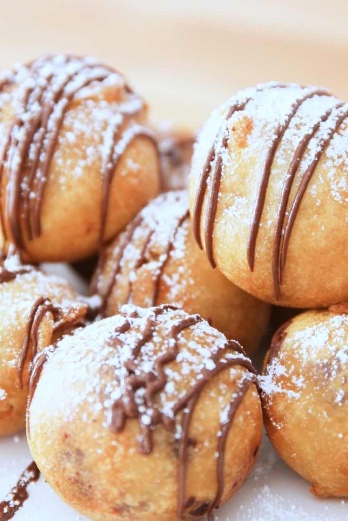 Closeup of golden Deep Fried Cookie Dough Bites drizzled with melted chocolate and dusted with powdered sugar