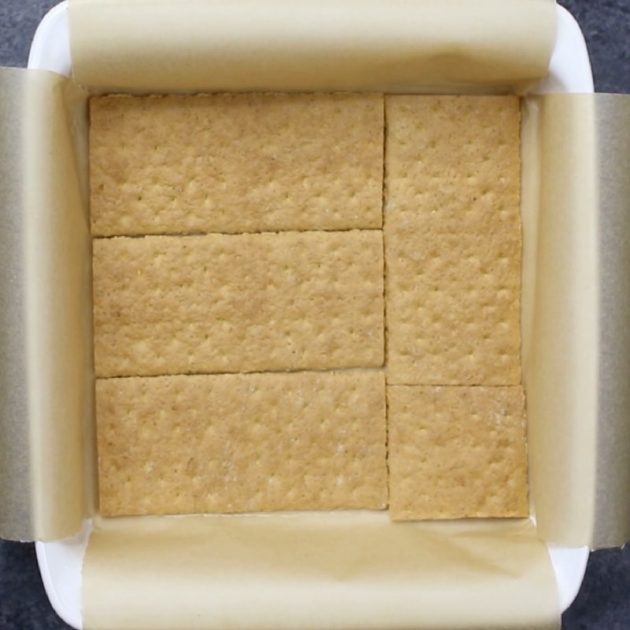 A square pan lined with parchment paper and graham cracker sheets